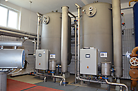 Zwei graue Zylinderfilter mit angeschlossenen Rohrleitungen, Steuerkästen und Ventilen in einem Technikraum.
